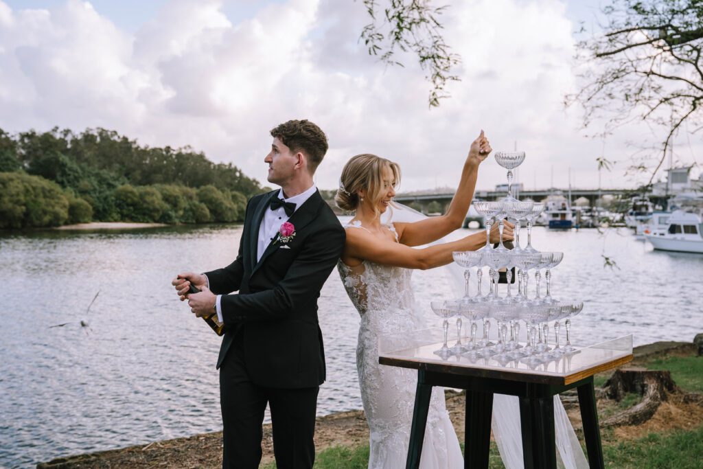 couple popping champagne for post-ceremony drinks at sunshine coast wedding by the lake