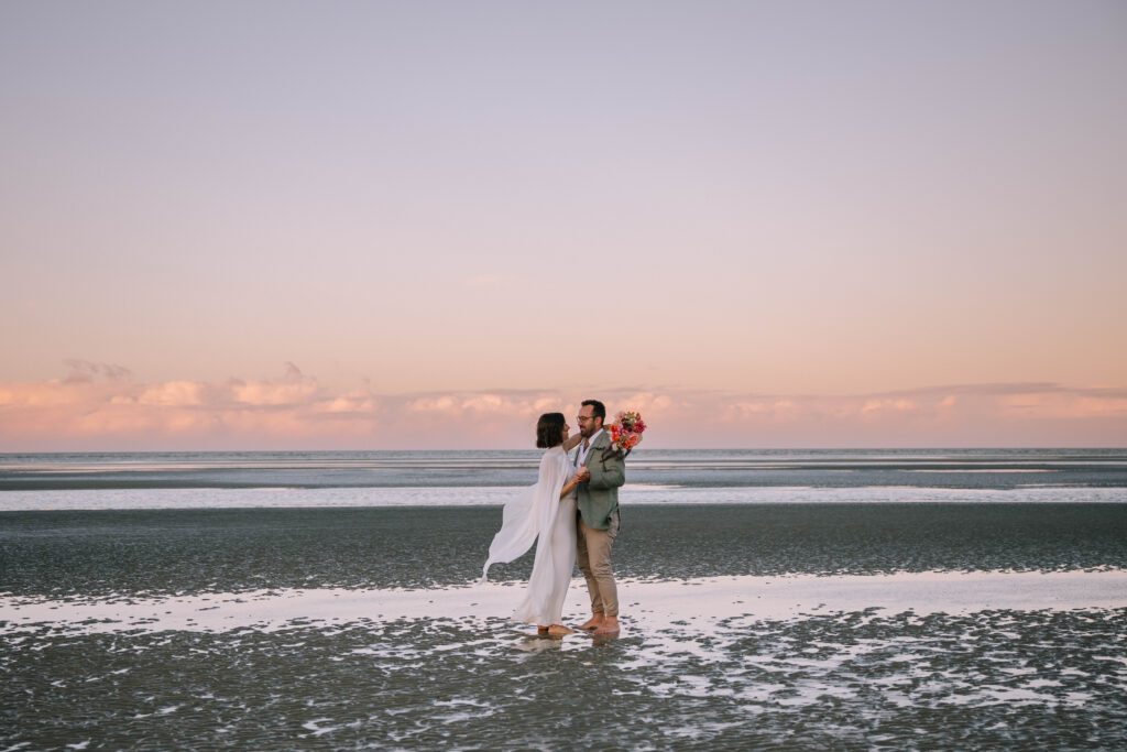 happy couple standing barefoot in the water on the beach after sunshine coast wedding ceremony