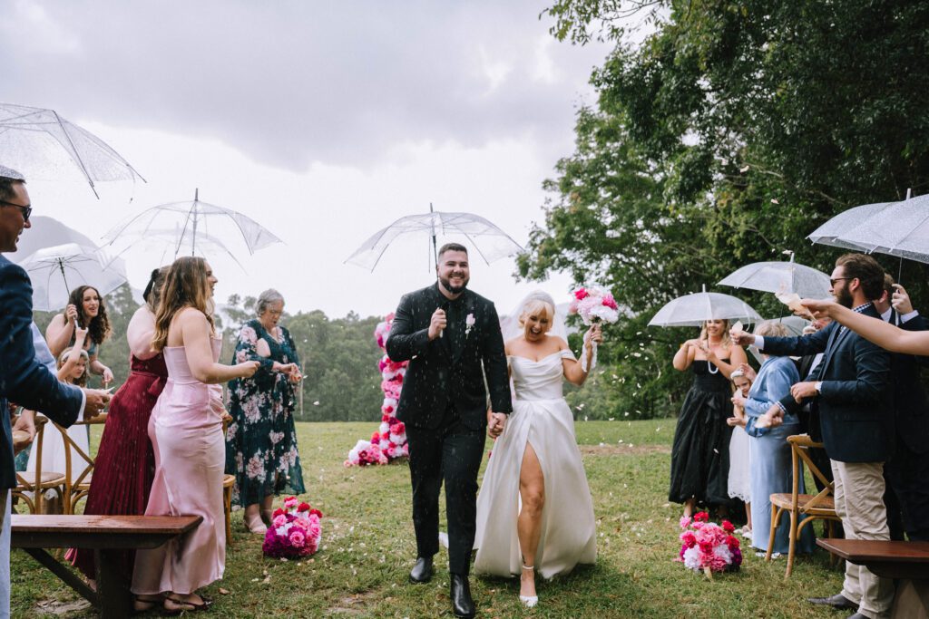 couple walking back down the aisle with clear umbrellas during rainy wedding ceremony on the sunshine coast