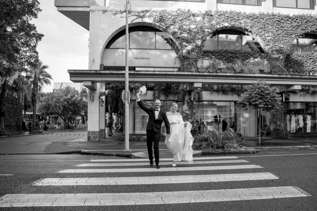 black and white candid portrait of bride and groom crossing at the zebra crossing