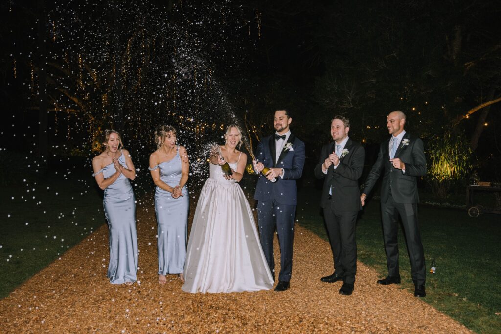 candid shot of couple popping champagne spray during wedding reception at gabbinar homestead 