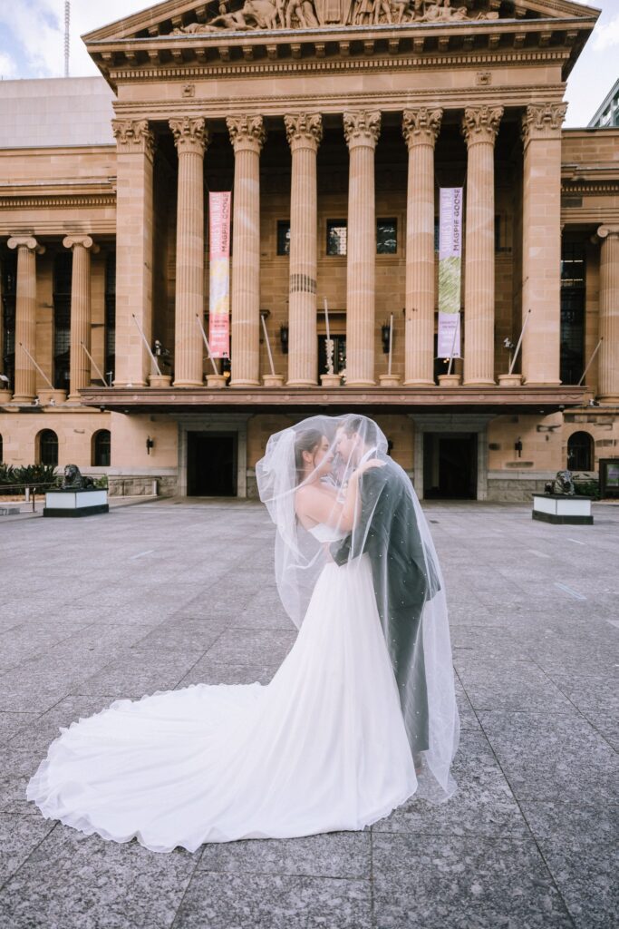 styled shot of couple kissing under bride's veil in front of heritage building