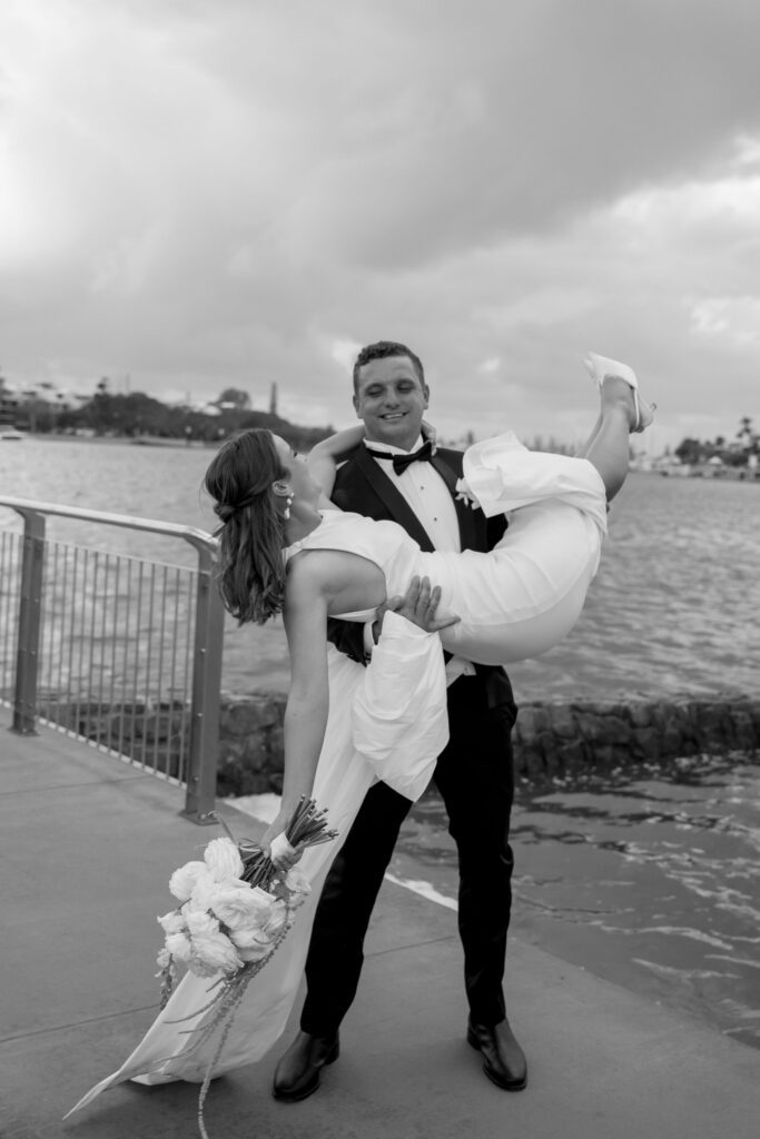 black and white candid portrait of groom lifting bride in the air during couple portraits 