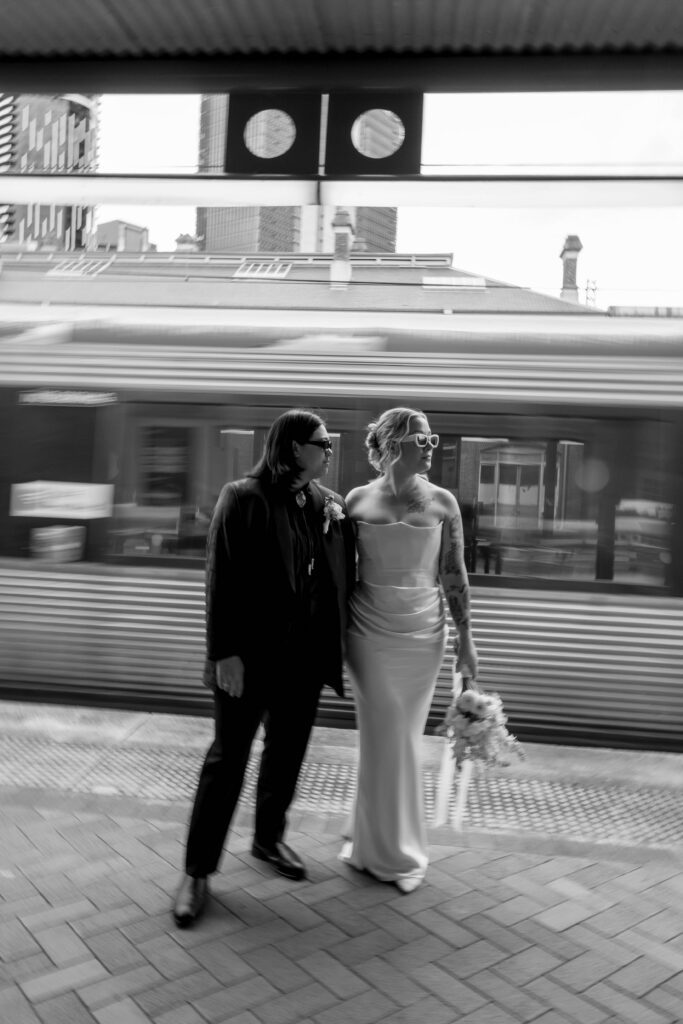 black and white editorial shot of couple holding hands with train flying past in the background 