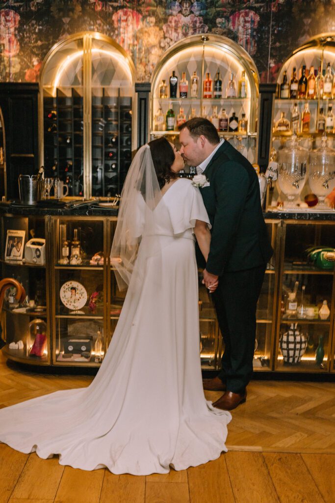couple kissing in front of brightly lit antique style bar at the inchcolm hotel wedding reception 