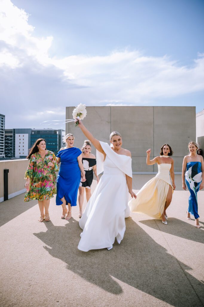 bride holding bouquet in the air with bridal party on the calile hotel rooftop