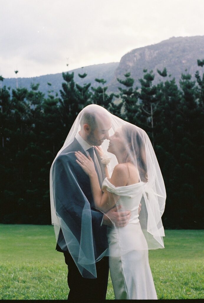 couple kissing under bride's veil in green field captured on 35mm film 