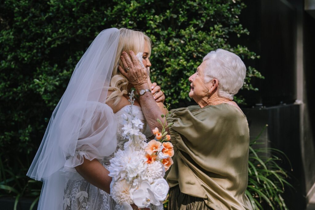 grandmother wiping away bride's tears during emotional first look before wedding ceremony 