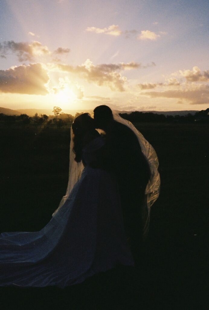stunning sunset shot of couple kissing in the field captured on 35mm film 