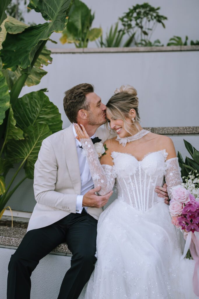 timeless portrait of groom kissing bride of the forehead while sitting outside Blackbird Bar Brisbane