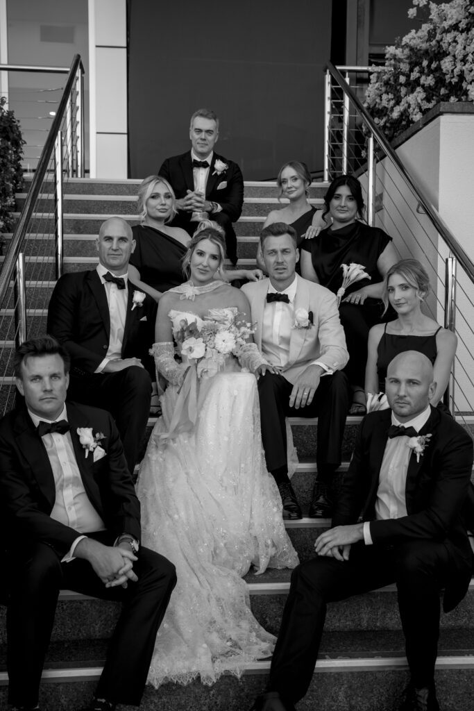 editorial black and white photography of couple sitting on steps with their wedding party
