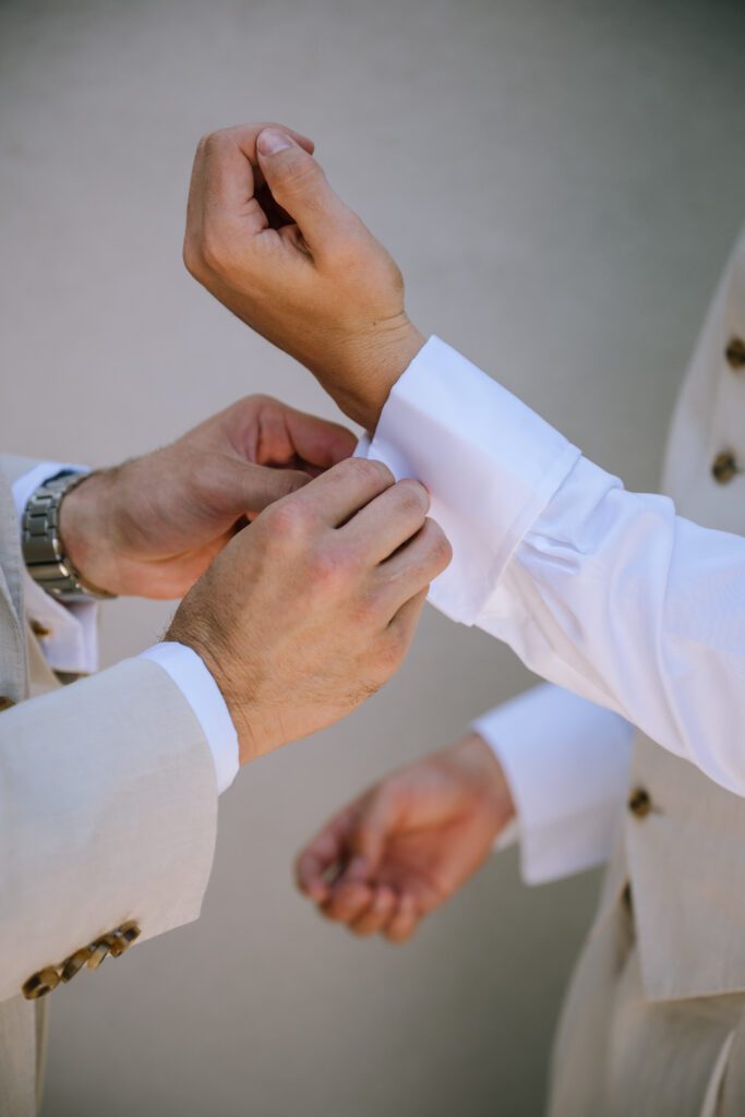 close up of groomsman helping groom put on cuff links while getting ready in the morning