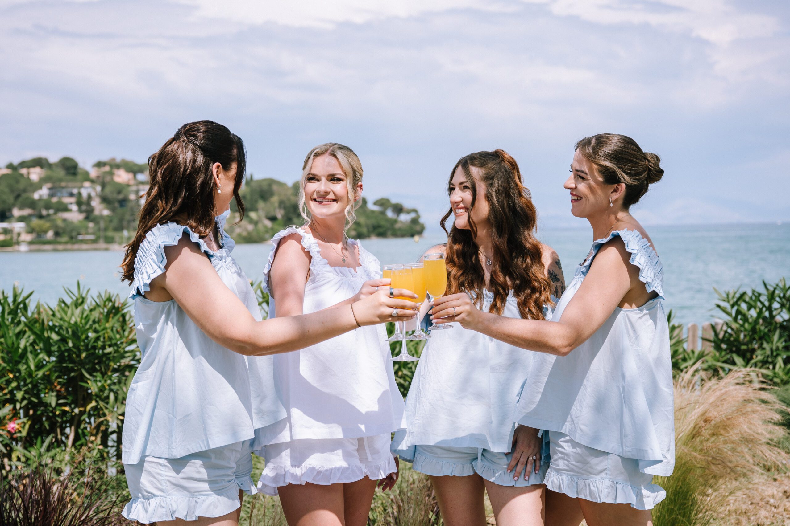 bride and bridal party enjoying cocktails in matching getting ready outfits with gouvia bay in the background