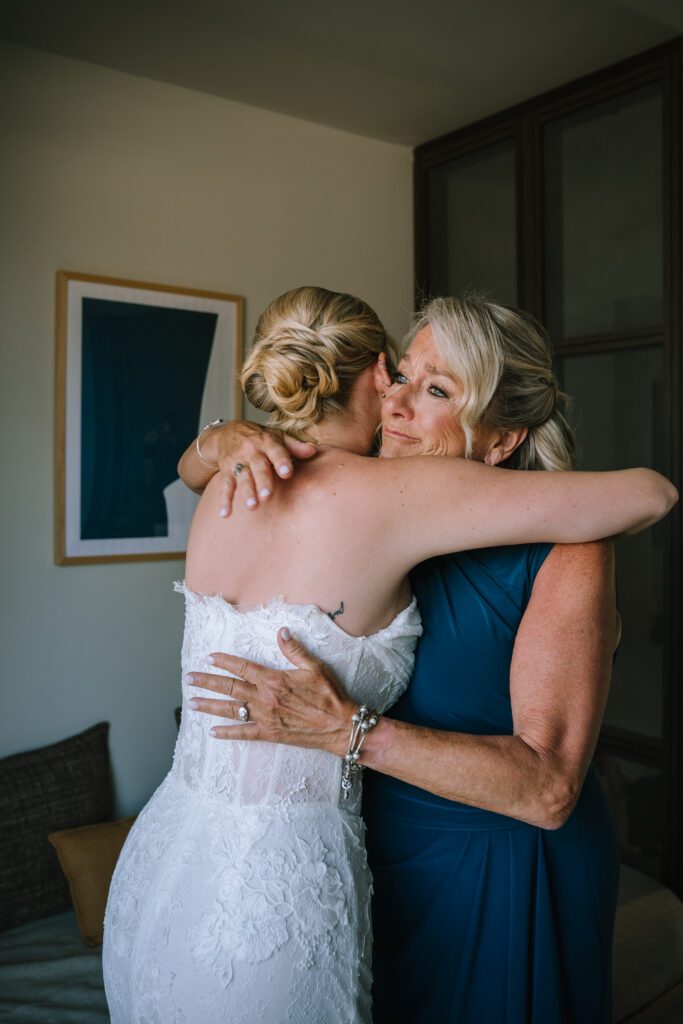 mum tearing up as she hugs the bride in the hotel room before the ceremony