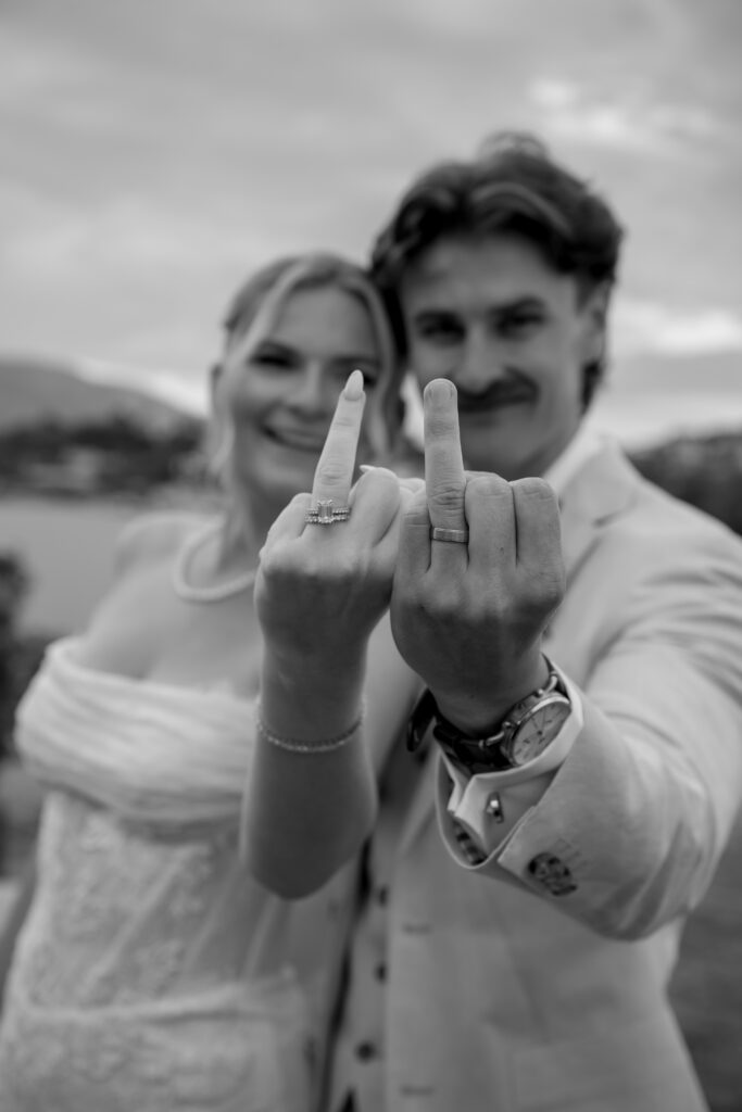 black and white shot of couple sticking their ring fingers up at the camera