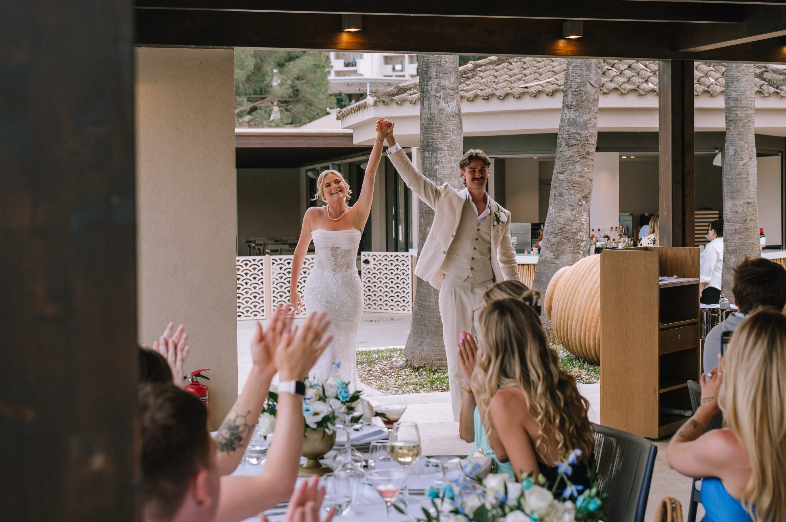 bride and groom arriving at the wedding reception with their arms in their air as guests cheer