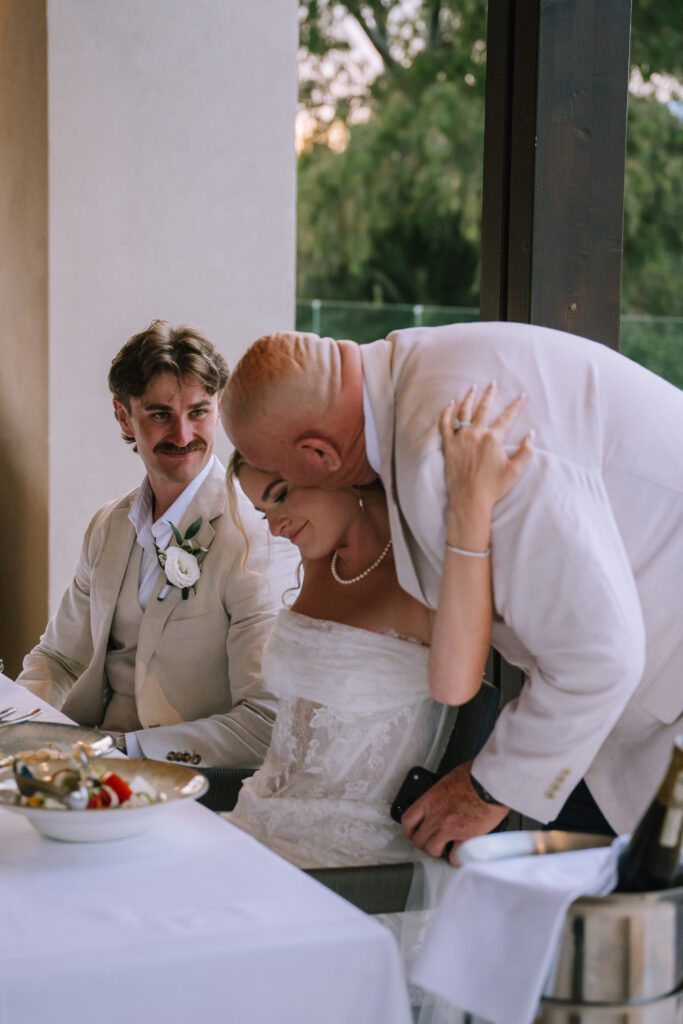 bride's father hugging her over the shoulder after wedding speech