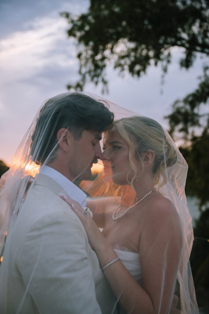 editorial portrait of couple embracing under bride's veil during golden hour