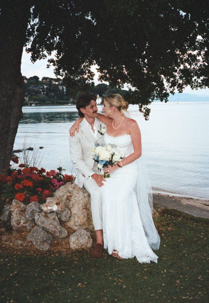 35mm film portrait of bride sitting on groom's lap next to red flowers in front of the bay