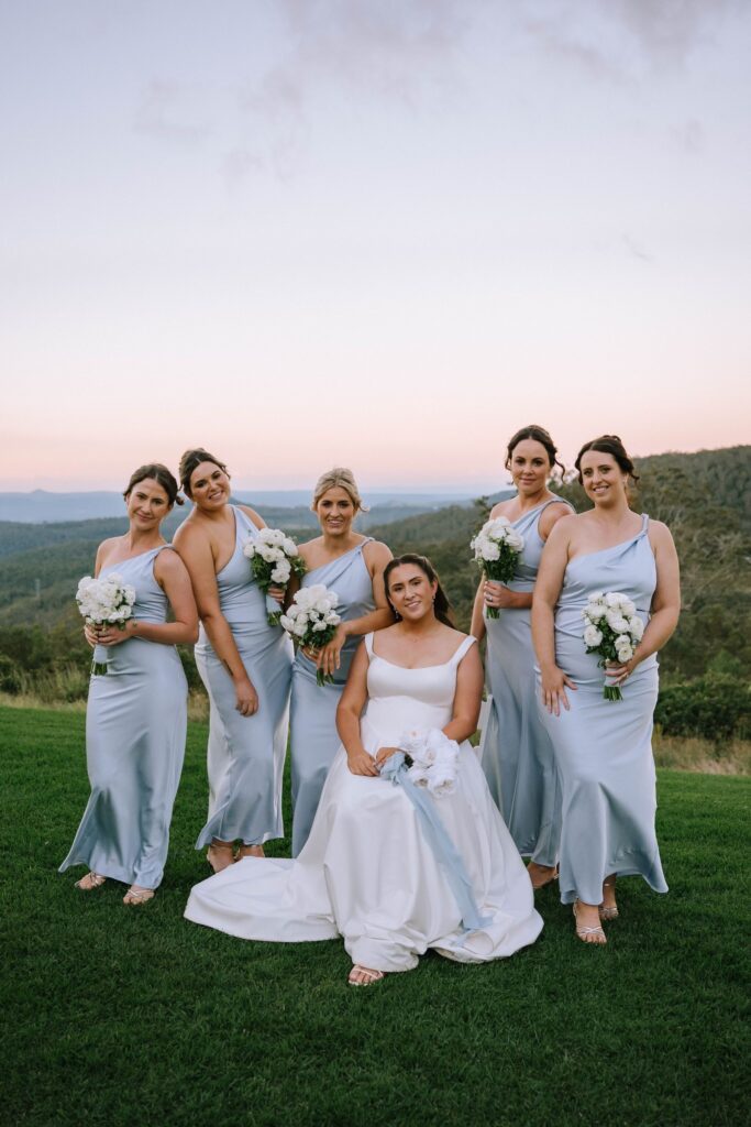 stunning outdoor shot of bride with bridesmaids in sky blue dresses, with lush hills and greenery