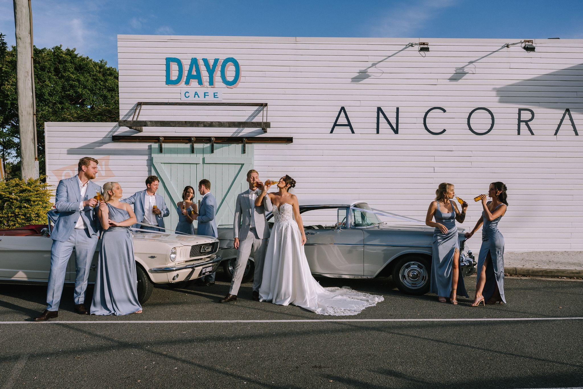 cool cinematic style portrait of couple and wedding party drinking beers next to vintage cars