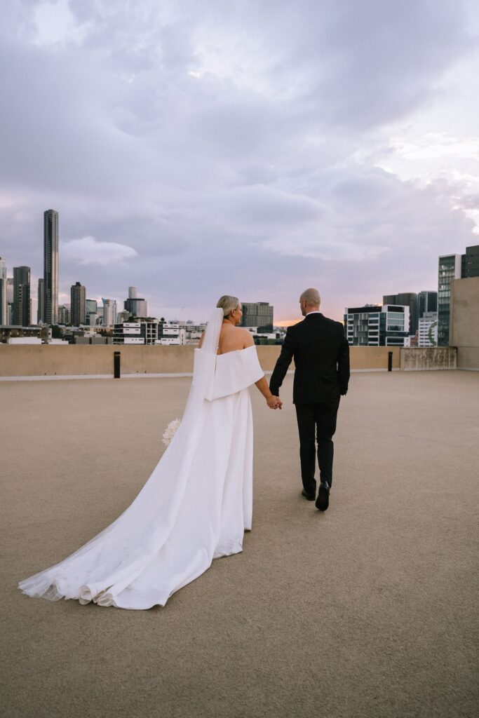 portrait session on rooftop capturing the bride and groom from behind as they walk towards city skyline